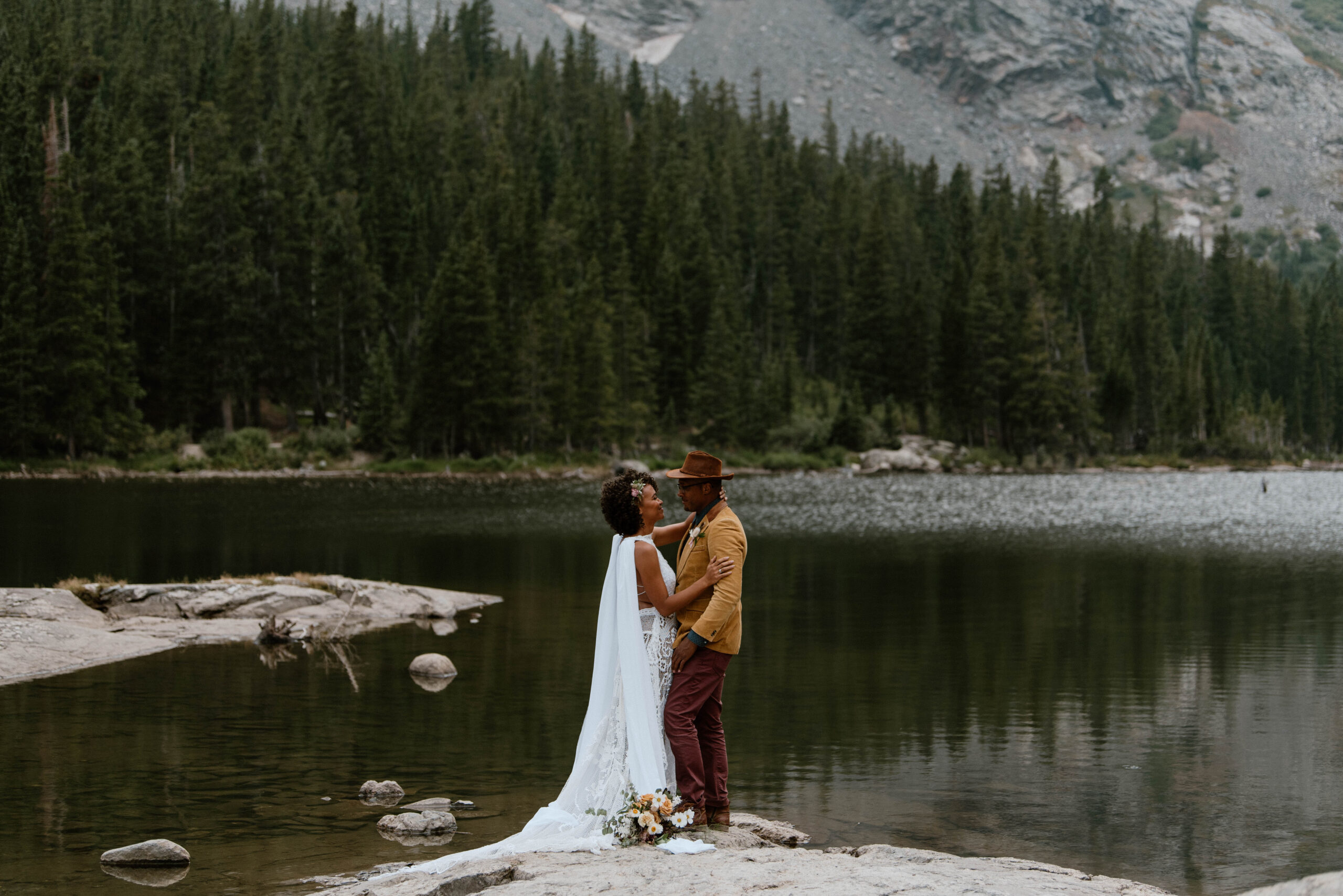 A couple embraces near an alpine lake after their Colorado wedding