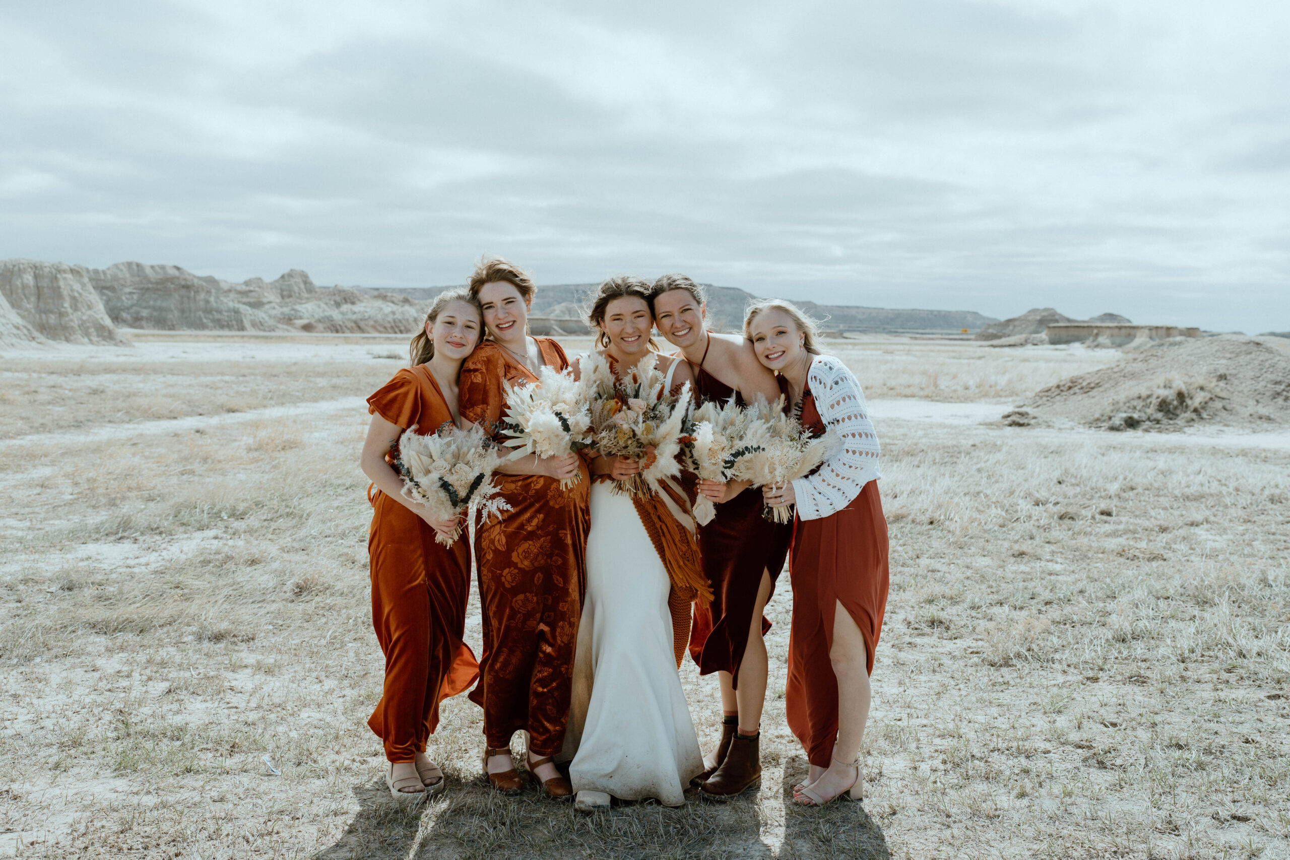 A bridal party is pictured with the bride and wearing burnt orange wedding attire