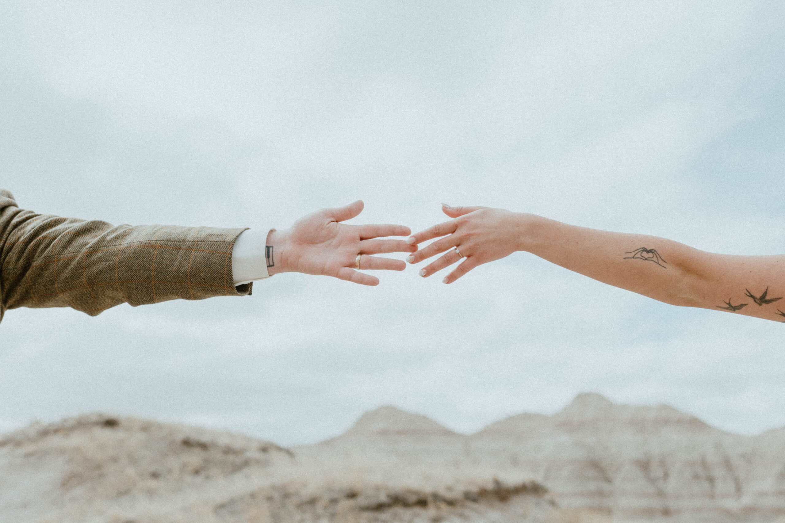 A bride and groom's hands are shown against a rugged landscape background in a national park elopement