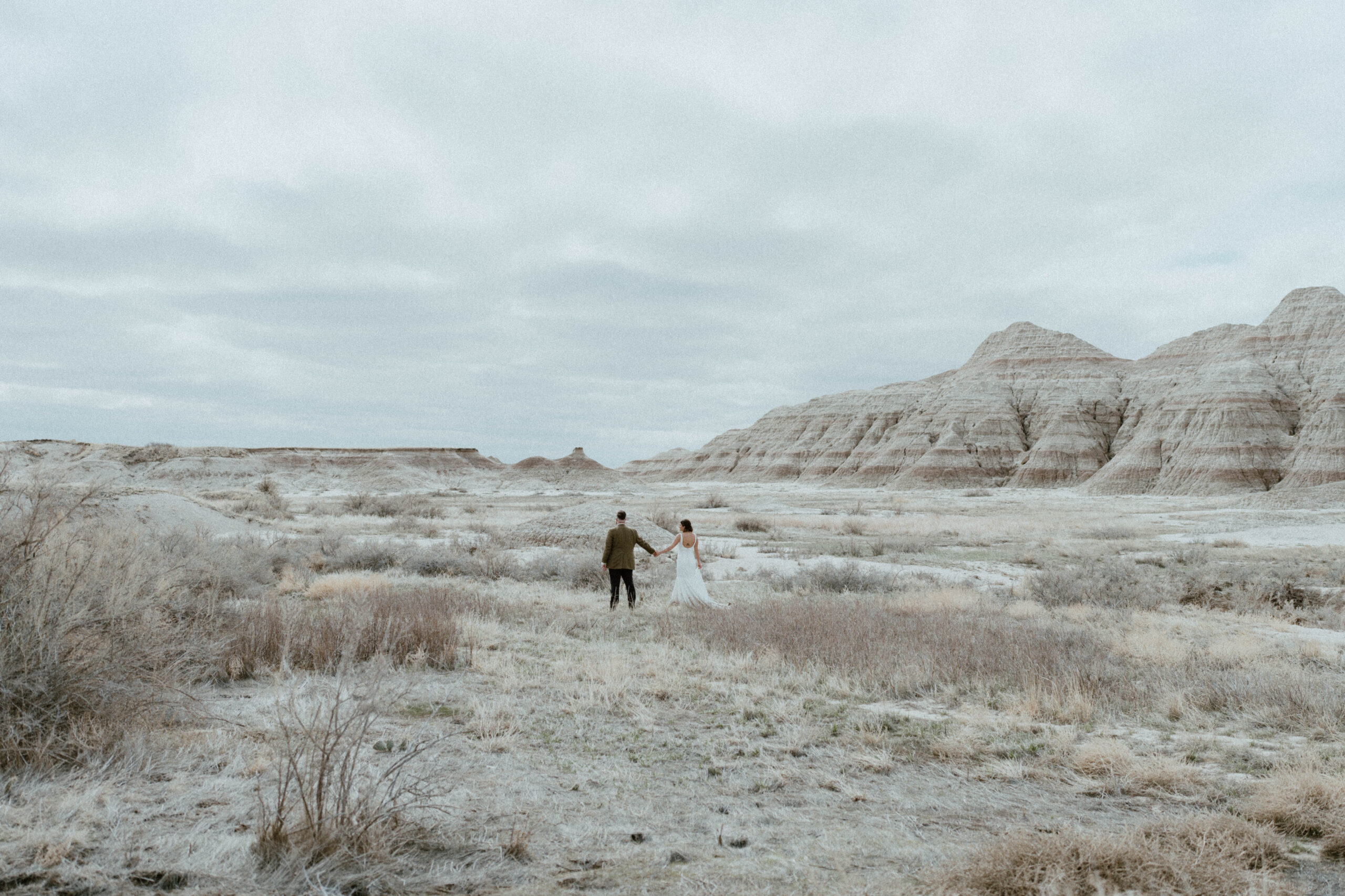 Newlyweds hold hands in a field in Badlands National Park