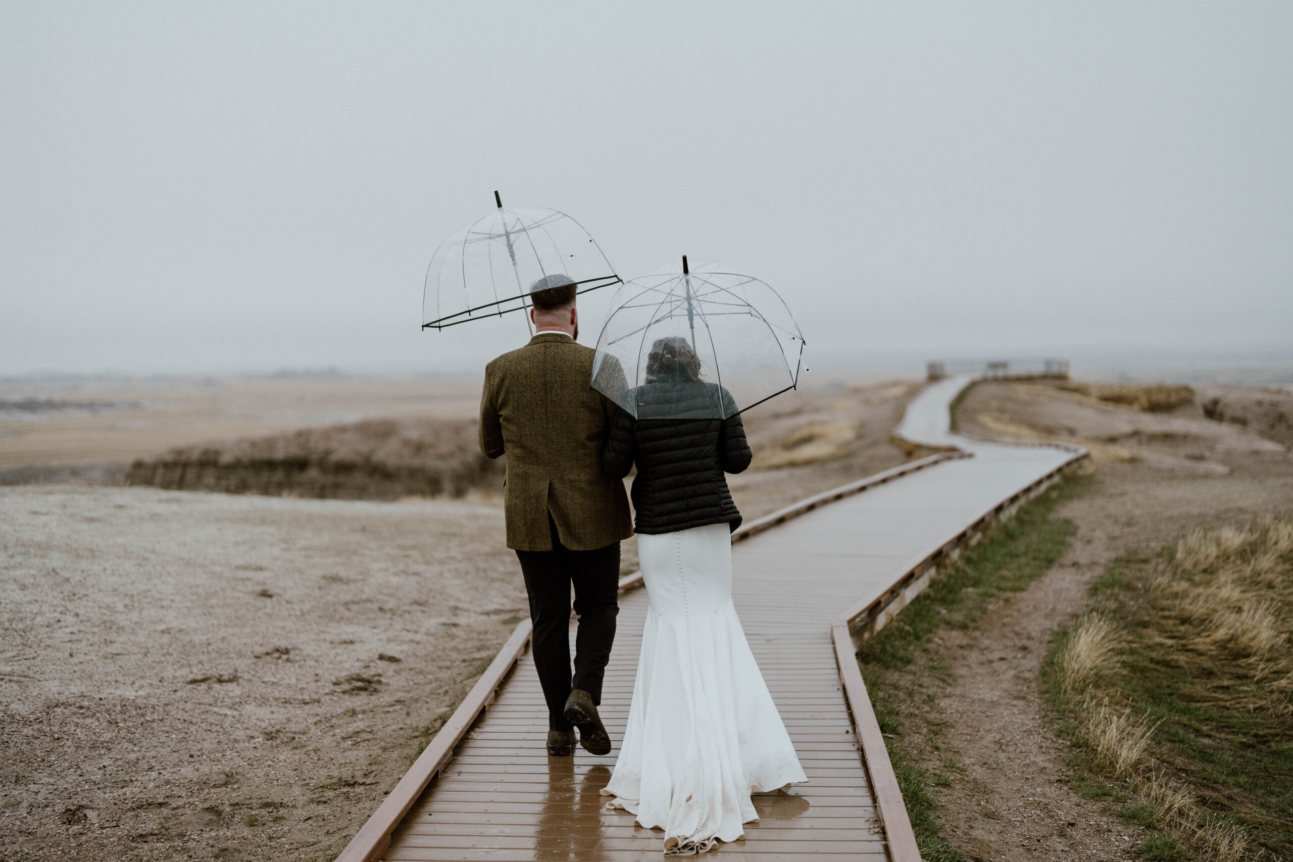A bride and groom walk in the rain before their hiking elopement