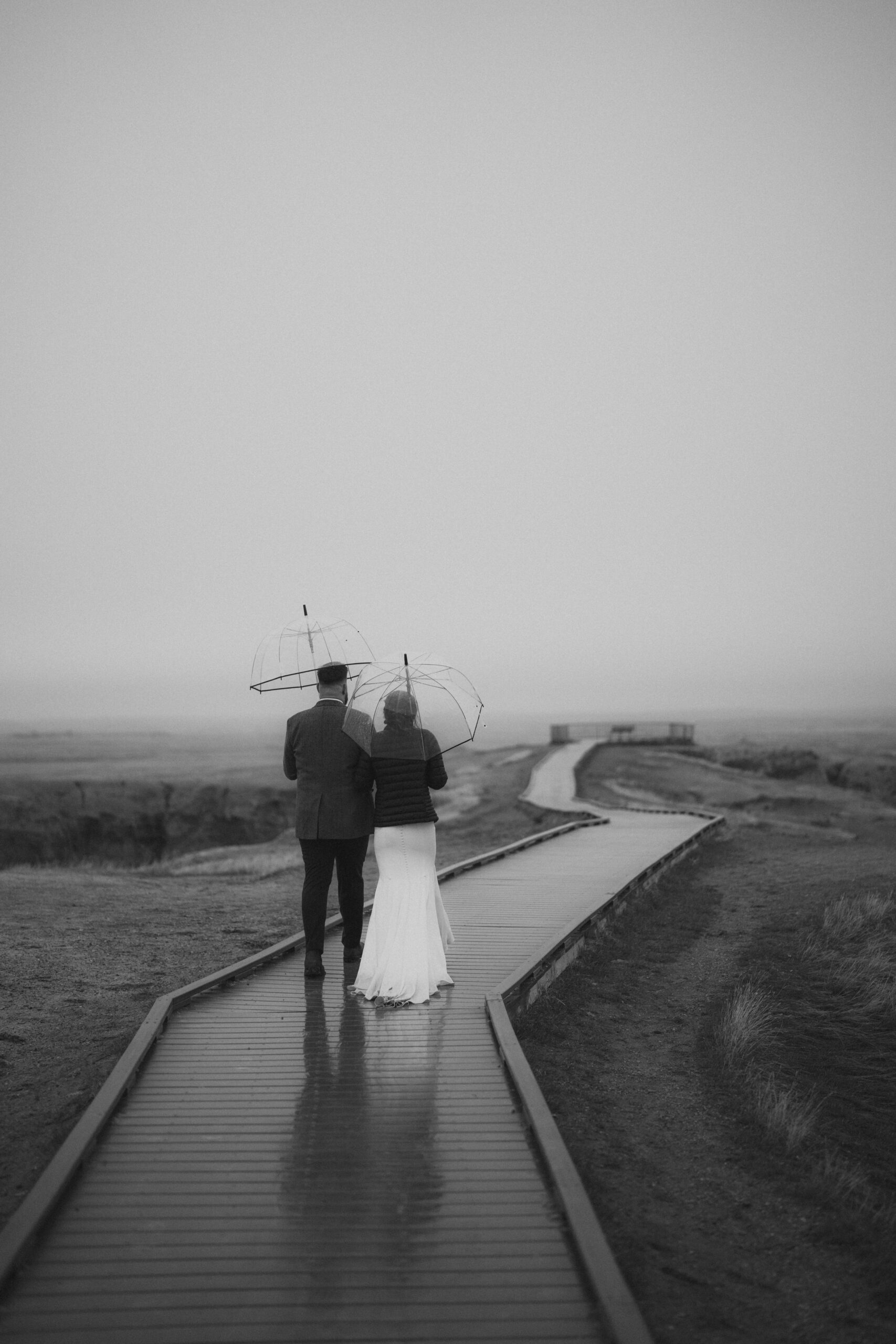 A couple walks side by side in the rain while holding umbrellas in Badlands National Park