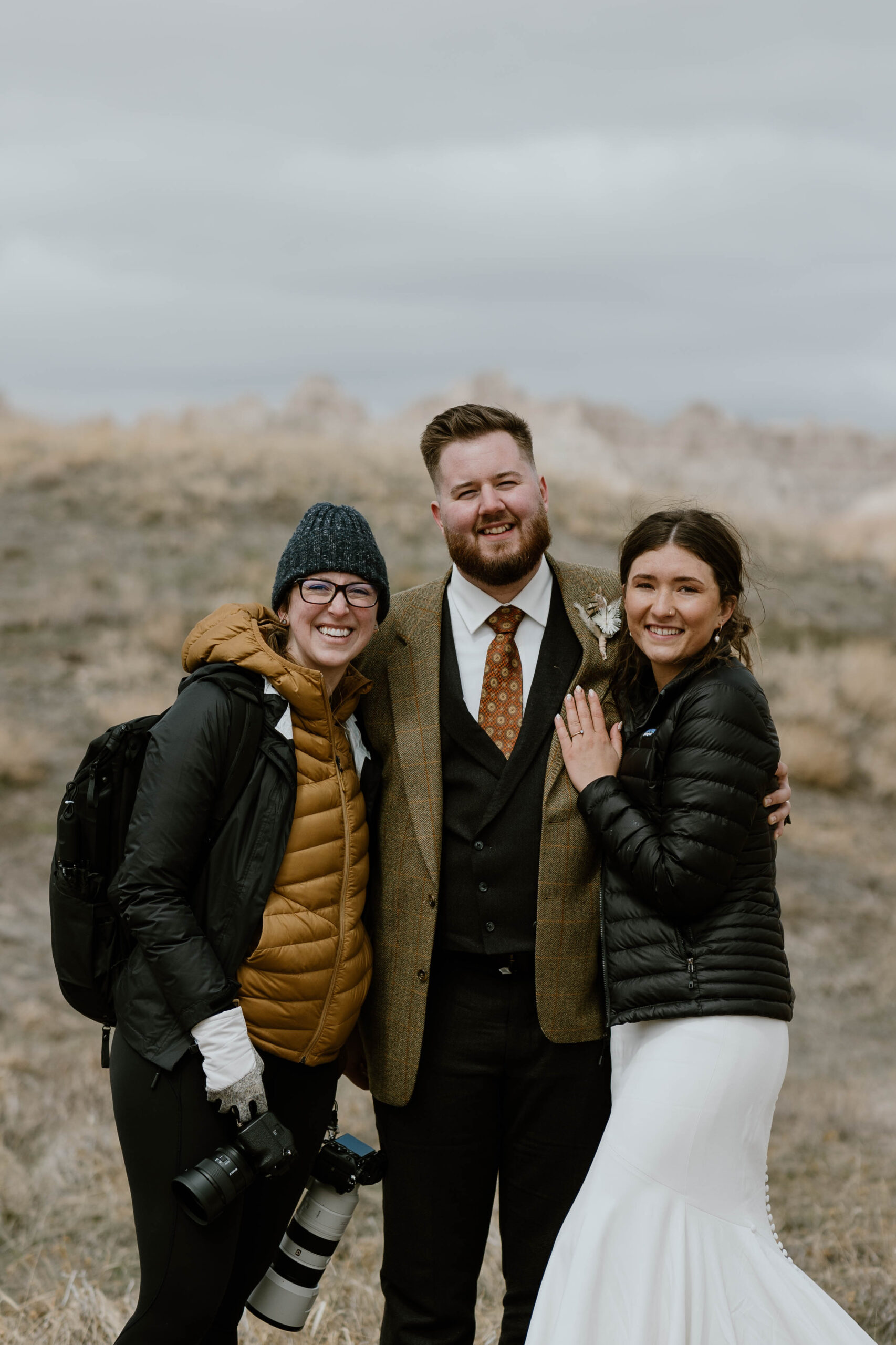 An elopement photographer poses with a couple before their elopement in Badlands National Park