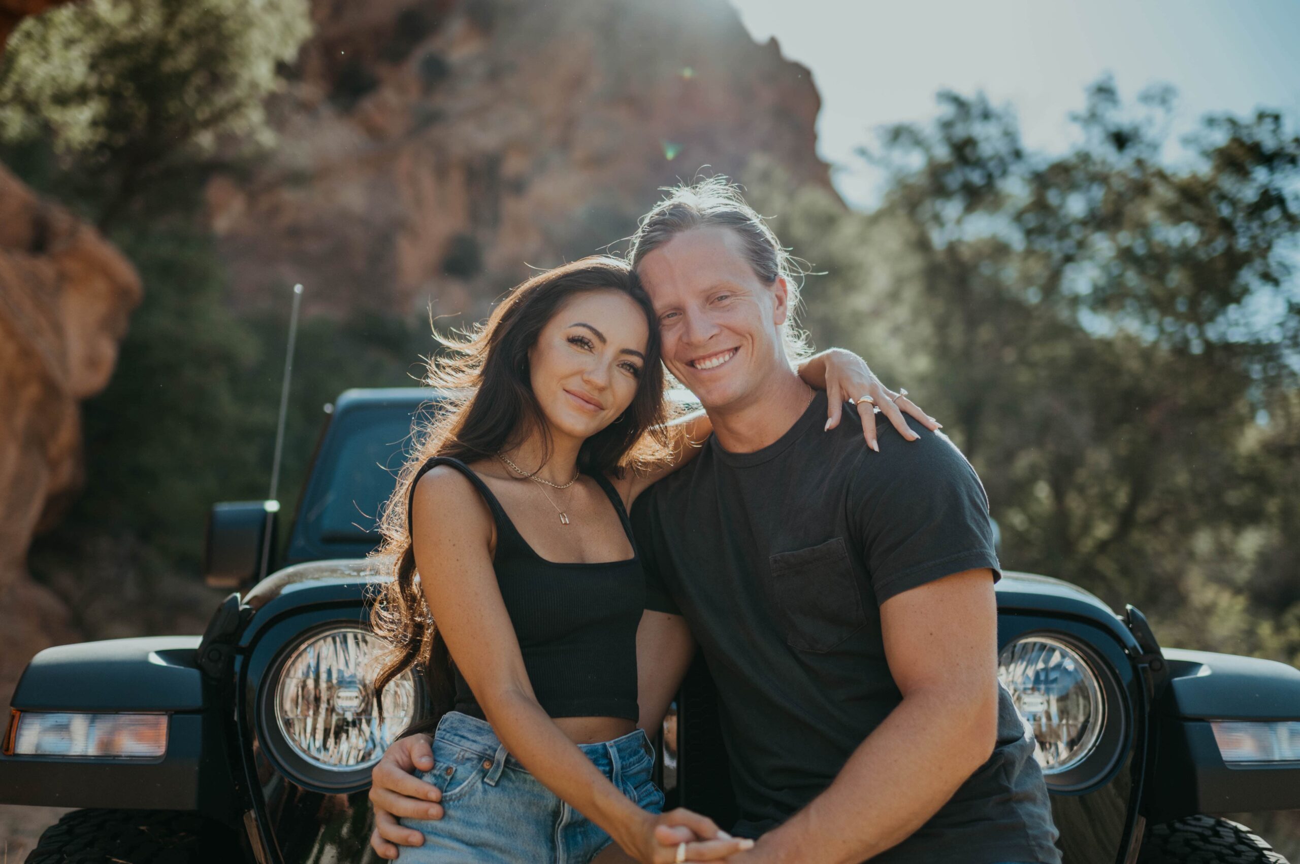 A couple smiles while standing in front of a Jeep outdoors