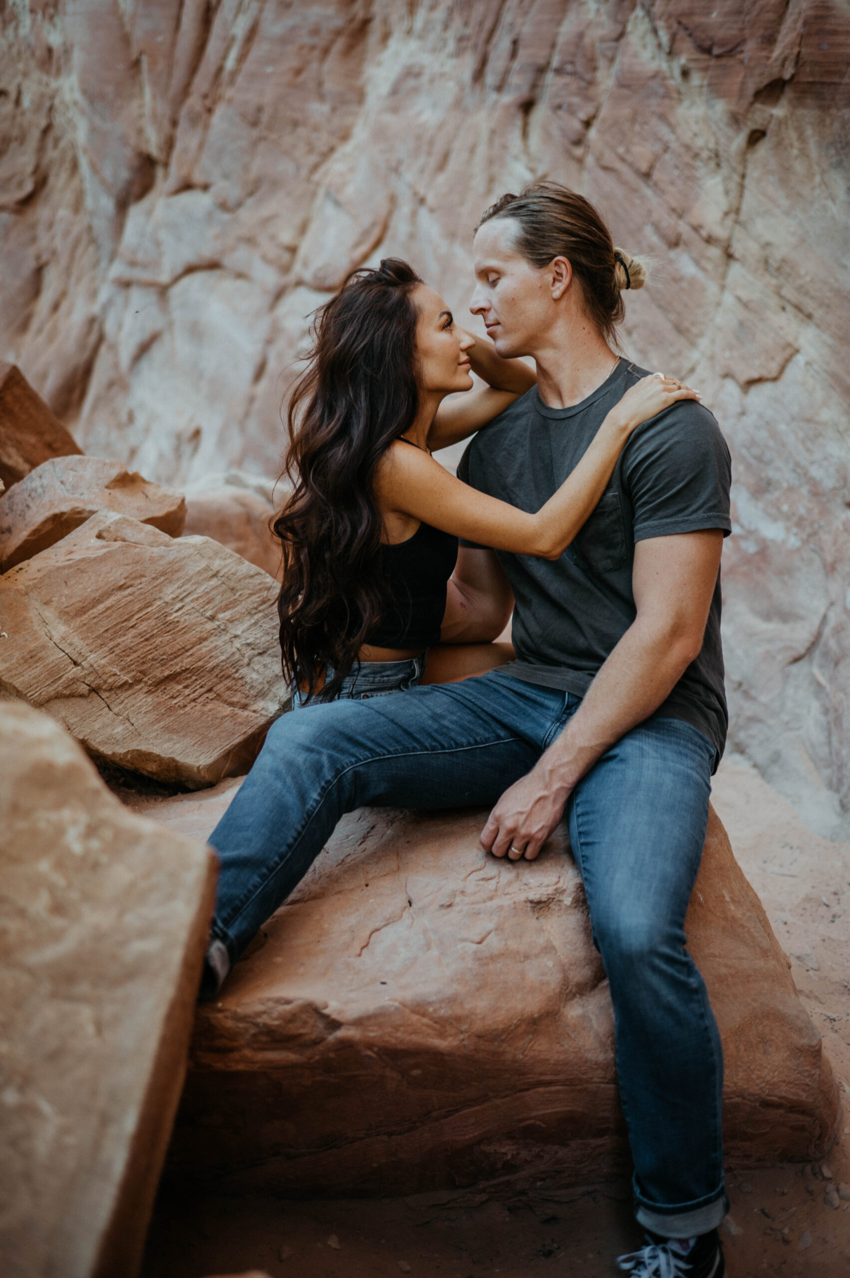 A couple sits on a red rock boulder in a canyon in Utah