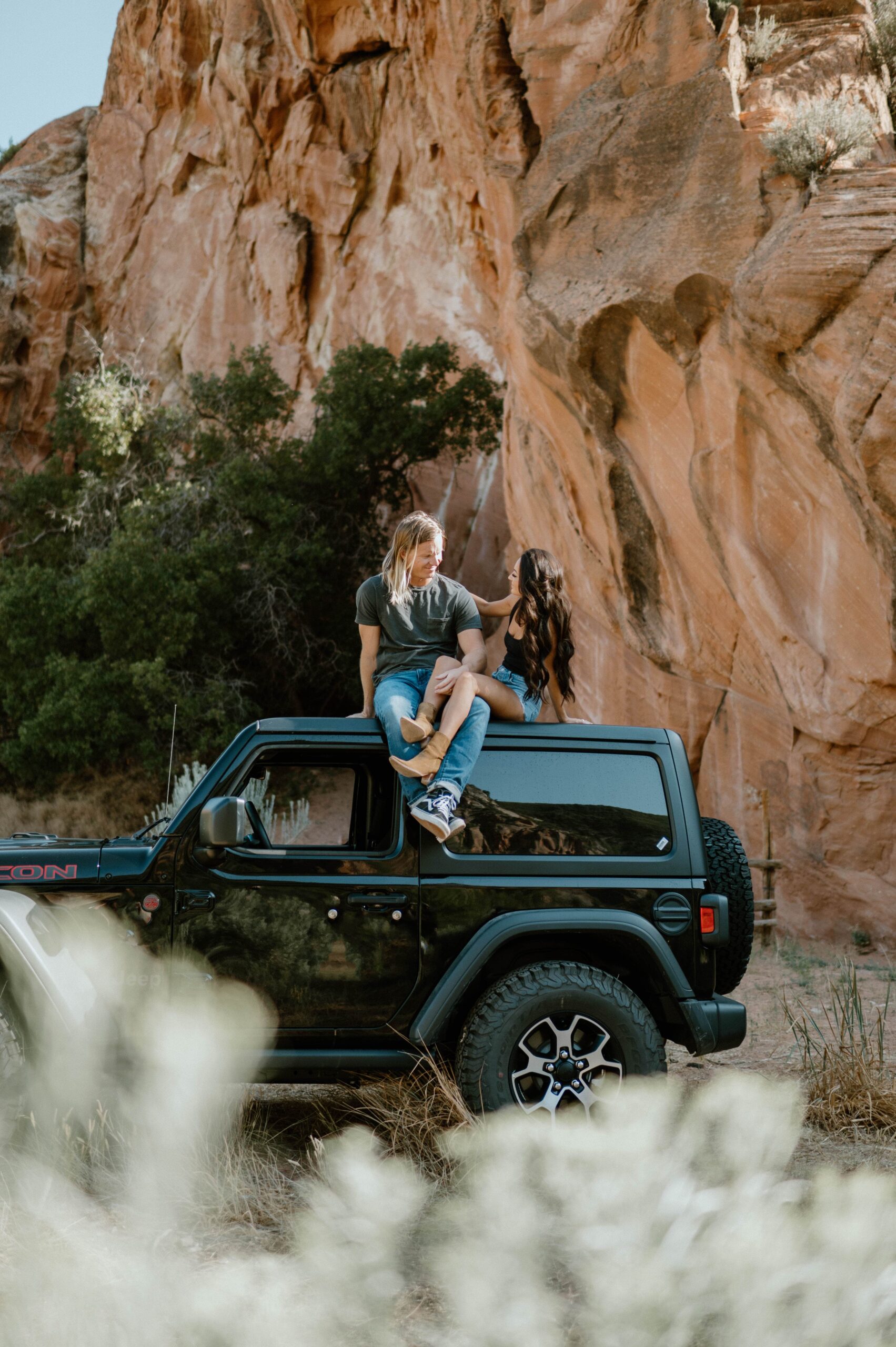 A couple sits atop a Jeep near red rocks in Utah