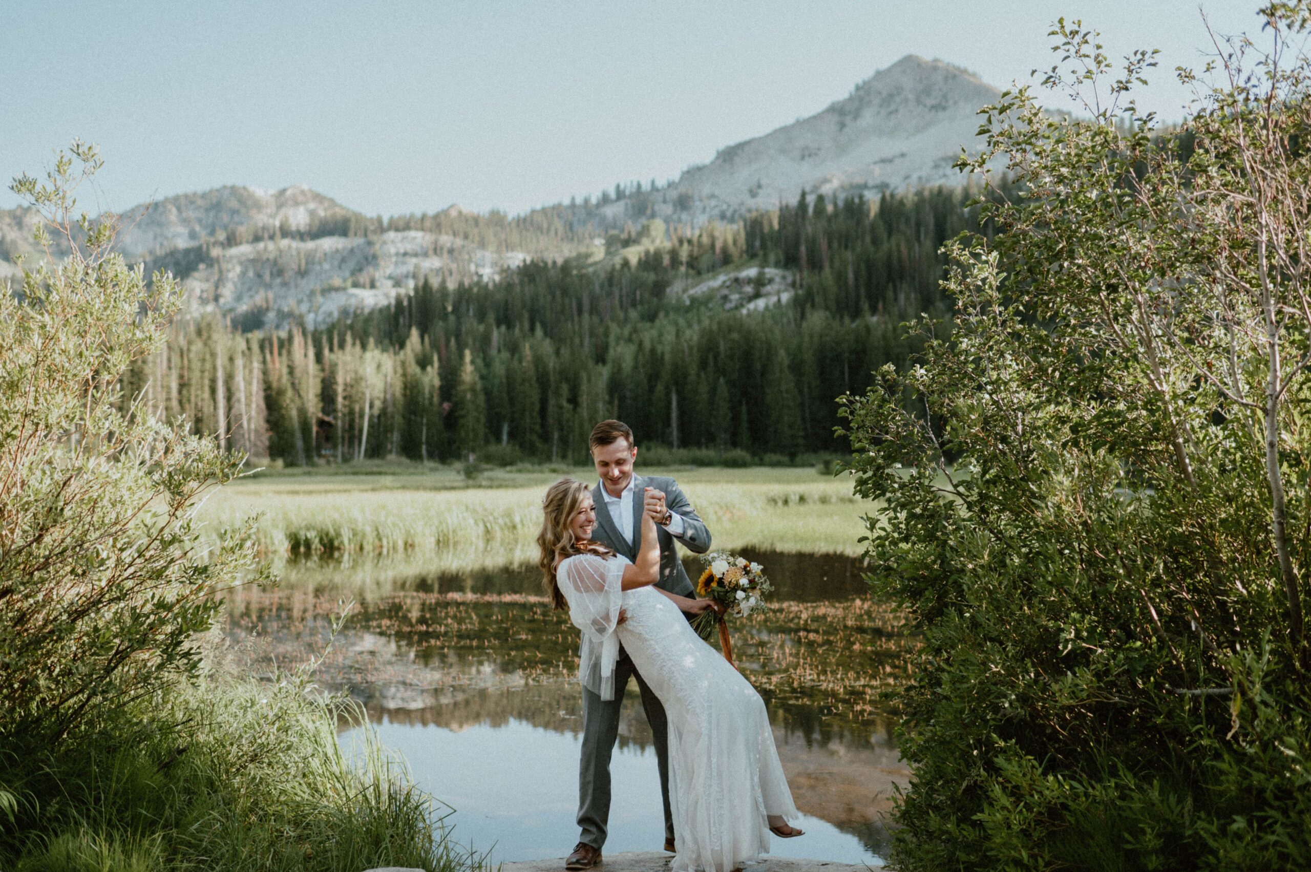 A groom dips his bride near a lake in Utah