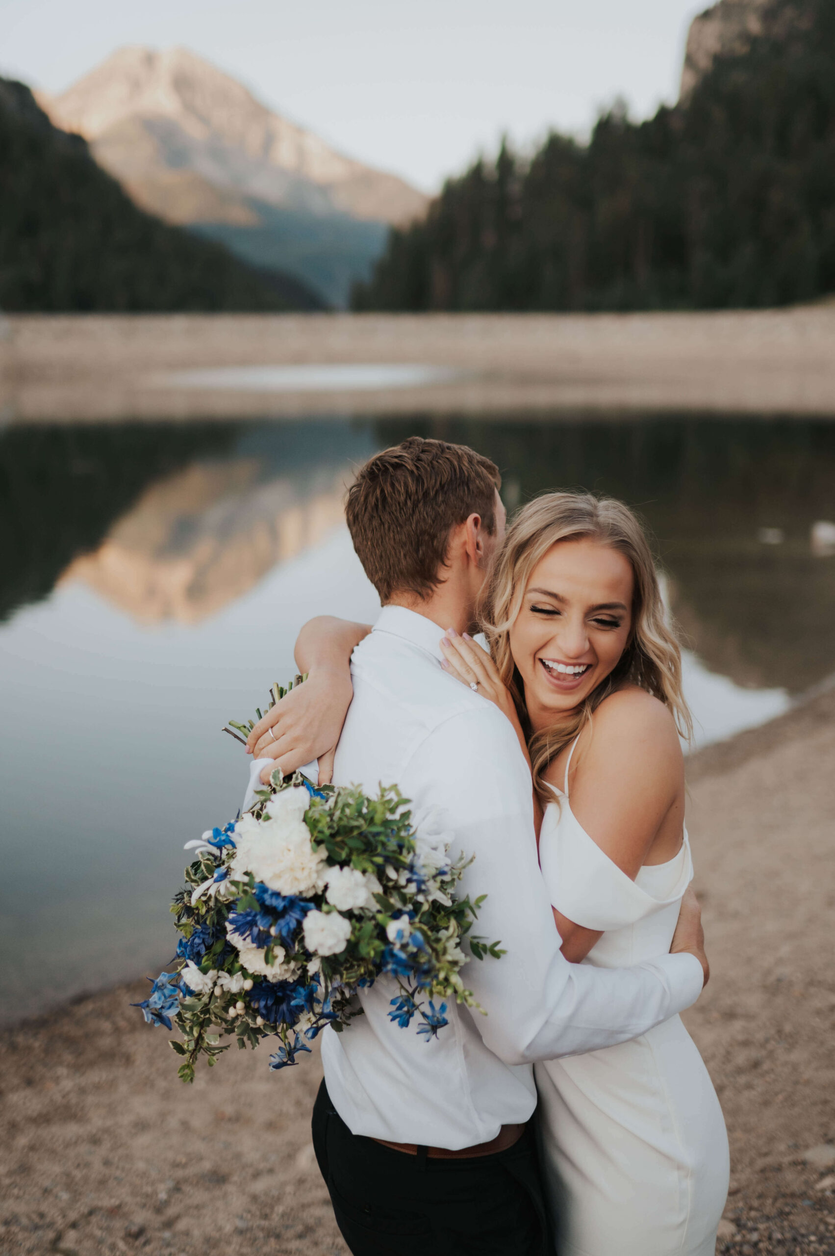 A bride and groom stand near a lake's edge during a Utah elopement