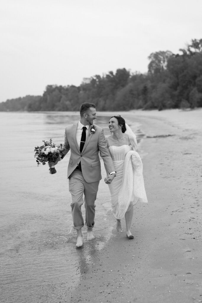 Newlyweds Garrett and Bailee walking along Selner Park Beach in Kewaunee, Wisconsin for their elopement portraits
